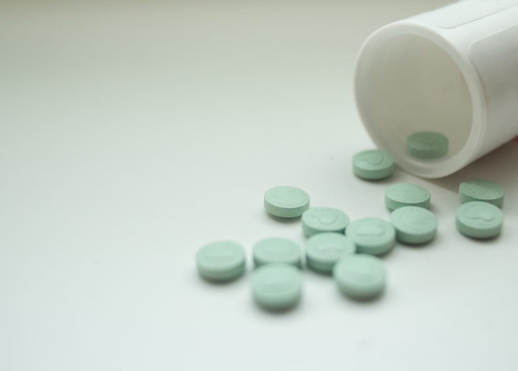 Green Pills Spilling from a White Pill Bottle