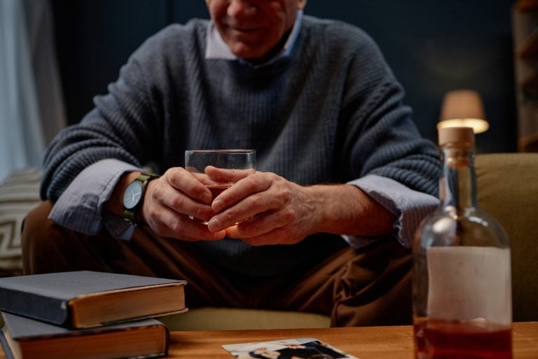 Man holding a glass of brandy, he is drinking alcohol in a room